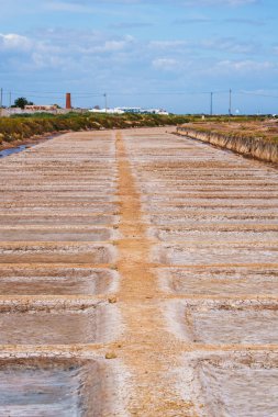 Kuru tuz kapları arka plandaki eski bir bacanın yakınına kadar uzanıyor..