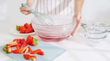 Çilek suyunu büyük bir cam kaseye karıştırmak için çırpma aleti kullanılıyor..