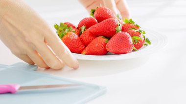 Eller kesme tahtası ve bıçağın yanında çilek tabağını kaldırıyor..