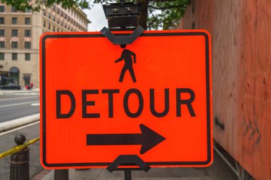 Parlak turuncu yaya yolu tabelası. Şehir kaldırımında sağdan gösterilen bir ok var..