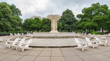 Washington D.C., ABD - 21 Mayıs 2025. Taş basamaklar ve beyaz sandalyeler bulutlu gökyüzünün altındaki Dupont Çemberi çeşmesinin etrafını sarar..