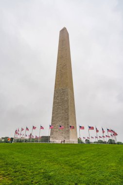 Washington D.C., ABD - 21 Mayıs 2025. Geniş yeşil çimlerin üzerinde Amerikan bayraklarından oluşan bir halka olan Washington Anıtı kuleleri.