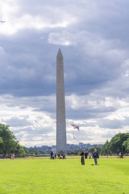 Washington D.C., ABD, - 23 Mayıs 2025, insanlar bulutlu bir gökyüzünün altında rüzgarda uçuşan renkli bir uçurtma gibi Washington Anıtı 'nın yanında toplandılar..