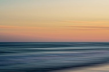 Bulanık dalgalar ve ufukta sıcak renkler olan soyut günbatımı sahnesi.