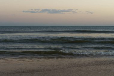 Şeftali rengi ve mavi gökyüzünün altında yumuşak bulanık okyanus dalgaları.