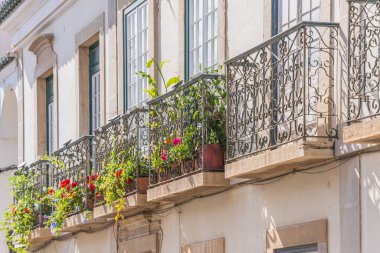 Dekoratif işlenmiş demir balkonlar renkli çiçekler ve tarihi bir Akdeniz binasının ön cephesinde saksı bitkileriyle dolup taşıyor..