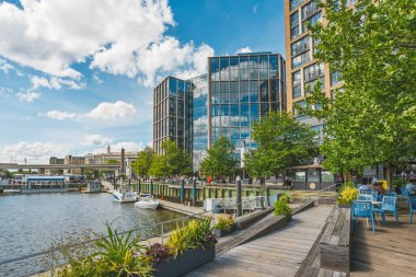 Washington D.C., ABD - 24 Mayıs 2025. Yayalar nehir kıyısında gökyüzünü yansıtan modern cam binalarla rahatlatıcı bir gezinti yaparlar..