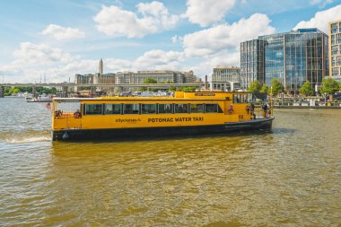 Washington D.C., ABD - 24 Mayıs 2025. Parlak sarı su taksisi arka planda şehir manzarası olan nehirde geziniyor..