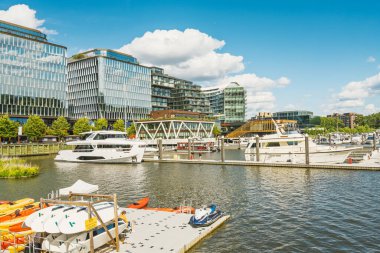 Washington D.C., ABD - 24 Mayıs 2025. Washington 'daki The Wharf' taki canlı marina lüks yatlar, yüzen rıhtımlar ve parlak mavi gökyüzü altında parlak modern binalar sergiliyor..