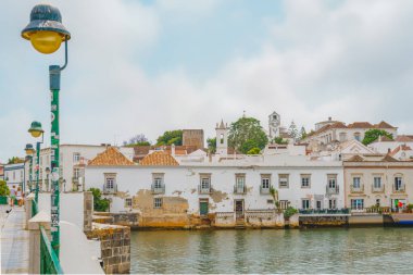 Tavira, Portekiz, 8 Haziran 2025. İnsanlar Roma Köprüsü 'nü geçerek Gilao Nehri' nin üzerinden geçiyor. Arka planda tarihi beyaz boyalı binalar var..