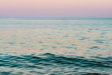 Bulanık deniz dalgaları, alacakaranlıkta yumuşak pastel yansımalarla harmanlanır..