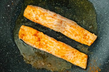 Yapışmayan tavada kızgın yağda pişen iki altın sarısı somon filetosu..