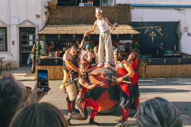 Castro Marim, Portekiz, 29 Ağustos 2025. Sokak oyuncularından oluşan bir grup, panayırda kraliyet figürü gibi giyinmiş gülümseyen bir çocuğu kaldırıyor..