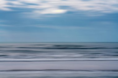 Bulanık dalgaları ve yumuşak çizgili bulutları olan soyut deniz manzarası.