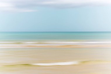 Pastel renkler ve hareket bulanıklığı dingin ve ruhani bir sahil manzarası yaratır..