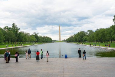 Washington D.C., ABD - 23 Mayıs 2025. Ziyaretçiler, suyun karşısındaki Washington Anıtı manzaralı Yansıyan Havuz 'un kenarında duruyorlar..
