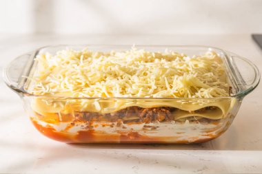 Cam bir tabak tamamen birleştirilmiş lazanya dilimlenmiş peynirle kaplanır ve pişirilmeye hazırdır..