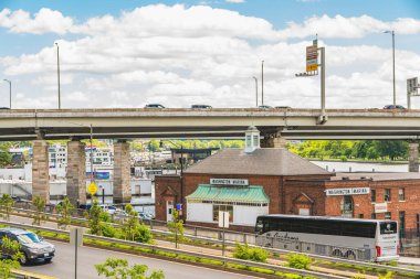 Washington D. C., USA - May 24, 2025. A large tour bus stops near the Washington Marina as cars pass above on a raised highway.