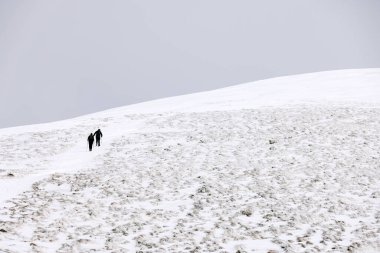 Trekking uphill in winter mountains, through snow and heading to mountaintop. Concept of mountaineering, alpinism and alpine climbing