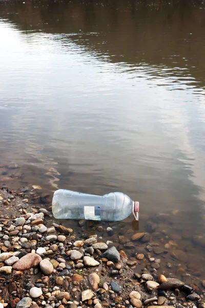 Water plastic pollution. Dirty plastic bottle and garbage on the river beach against the background of water. Environmental protection, ecology, nature concept.