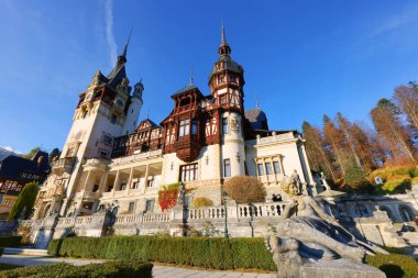 View of Peles castle with arranged courtyard and colorful autumn forest in Sinaia, Romania, Europe