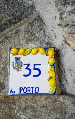 İtalya 'nın Limone Konsolosu Garda' nın eski taş duvarında mavi figürlü seramik fayans ev numarası. Geleneksel İtalyan ev tabelası seramik fayans üzerine boyanmış