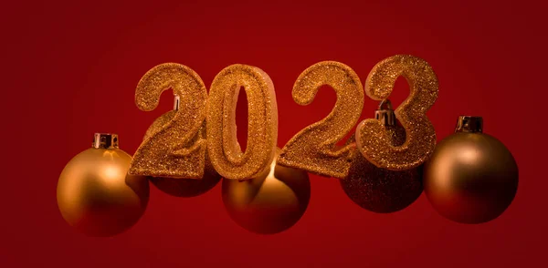 New Year banner with golden sparkling number 2023 and christmas balls against dark red color background.