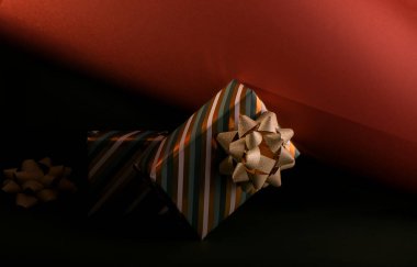 Boxing Day concept with gift boxes in gold and green colors decorated with sparkling bow against deep green and brick color paper background.