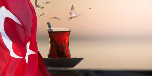 stock image Traditional Turkish Glass of Tea. Photo Collage with Seagulls flying over a glass of tea against the blurred background and the National Flag of Turkey. Good for Turkey's tourism promo banner