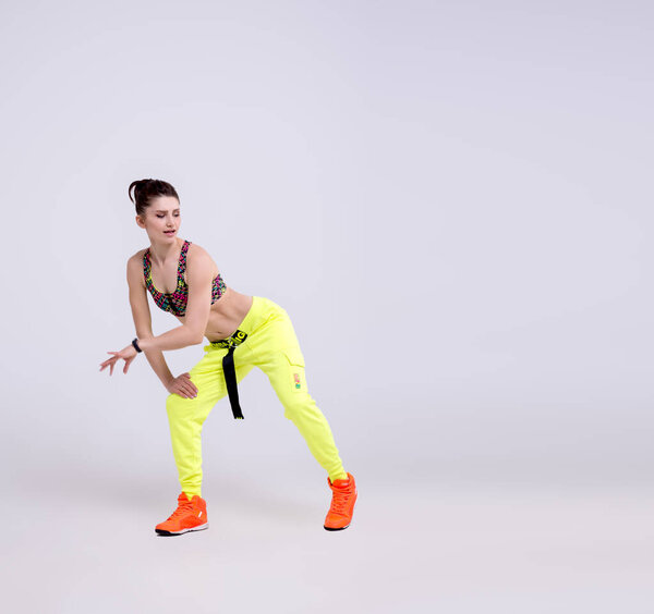 Attractive sporty woman wearing bright yellow pants jumping in the air against a white background. Dispersion and light flare effect on Womans body silhouette.