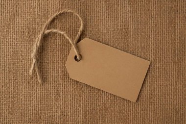 Çuval bezi arka planında sicim olan dikdörtgen kraft kağıt etiket. Çevre dostu paketleme konsepti. Sıcak stüdyo ışıkları. Yatay bileşim.