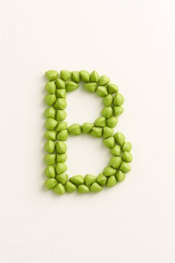 Yeşil karabuğday, beyaz bir yüzeyde büyük B şeklinde sıralanmış. Doğal ve sanatsal üst görünüm.