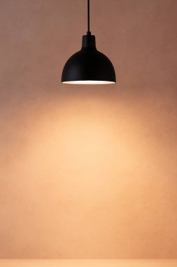 Dikey bir fotoğraf, yumuşak desenli bej bir duvara sıcak bir ışık saçan modern siyah bir kolye içerir. Altında mükemmel bir boşluk vardır. Metin veya damgalama için mükemmel..