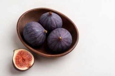 Parlak nötr bir arkaplan karşısında dört olgun incir içeren minimalist kompozisyon, yiyecek ve yaşam tarzı temaları için temiz ve taze bir estetik oluşturuyor..