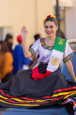 Matamoros, Tamaulipas, Meksika - 26 Kasım 2022: Desfile del 20 de Noviembre, geleneksel giysiler giyen Güzellik Kraliçesi ve omzunda Meksika bayrağı, seyircilere el sallıyor