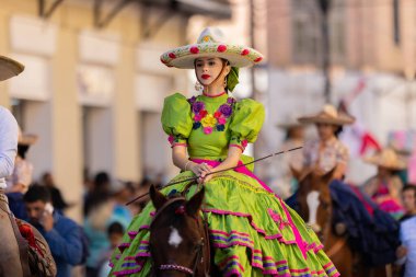 Matamoros, Tamaulipas, Meksika - 26 Kasım 2022: The Desfile del 20 de Noviembre, geleneksel charro kıyafetleri giyen genç bir kadın, geçit töreninde ata biniyor.