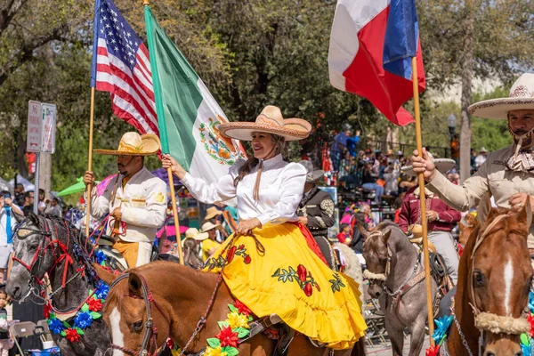 Stock image San Antonio, Texas, USA - April 8, 2022: The Battle of the Flowers Parade, Men and woman wearing traditional charro clothing, riding horses, carrying the mexican american and texan flags