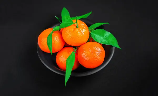 Fresh mandarin oranges fruit or tangerines with leaves on black background. Copyspace. Fresh picked mandarins Top view