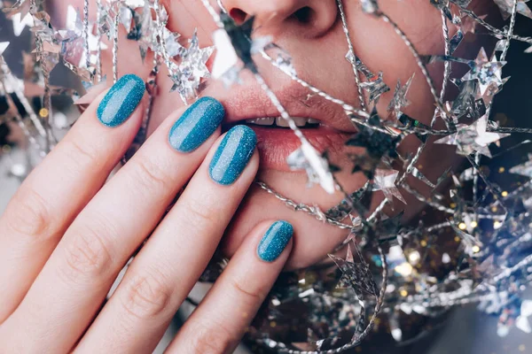 Beautiful woman with holiday manicure - blue glitter nails with silver twisted wire with stars. Closeup view. Nail care concept