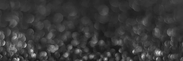 Gray black sparkling glitter bokeh background, abstract defocused texture. Holiday lights. Snowy shiny sparkle stars header. Wide screen wallpaper. Panoramic web banner with copy space