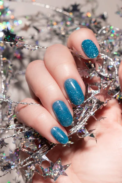 Female hand with beautiful holiday manicure - blue glitter nails with silver twisted wire with stars. Nail care concept