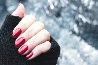 Siyah örgü eldivenli kadın eli. Güzel bir tatil manikürü olan eldivenler. Viva moru, gümüş Noel süslerinin arka planında bordo tırnaklar.