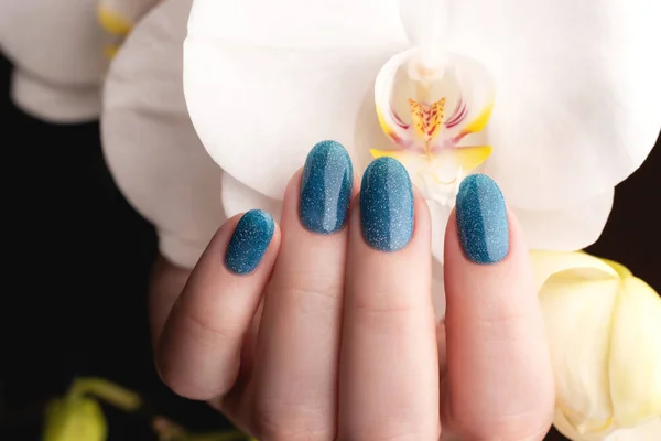 女性的手与美丽的指甲修整 蓝色闪亮的指甲与白色仙人掌兰花 指甲护理概念 — 图库照片