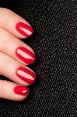 Güzel manikürlü bir kadın eli. Siyah deri arka planda kırmızı tırnaklar. Çivi bakımı kavramı