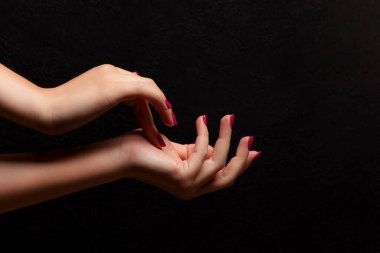 Female hands with beautiful manicure - viva magenta, pink nails on dark black background. Nail, skin care concept