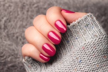Female hand with beautiful manicure - viva magenta nails on gray fluffy knitted fabric. Nail care concept