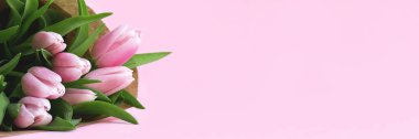 Beautiful delicate bouquet of tulip flowers in craft wrapping paper on pink background banner. Panoramic web header with copy space. Wide screen wallpaper