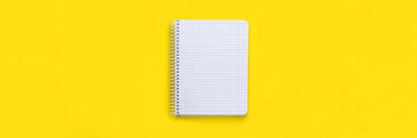 Open spiral squared notebook with blank empty white sheets on bright yellow background, top view banner, flat lay with copy space panoramic web header