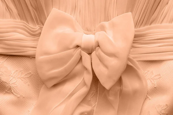 Delicate peach fuzz bow on wedding dress. Textile fabric decoration background.