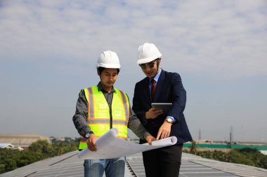 Güneş mühendisi ve teknisyen fabrikanın çatısında mavi baskı çizimi, güneş enerjisi yenilenmesi, güneş çatısı alanında çalışan mühendis ve iş adamı, güneş projesinde ilerleme
